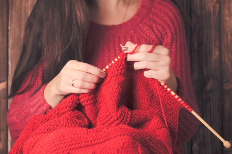 kvinne holder i pinner og strikker en rød, varm jakke